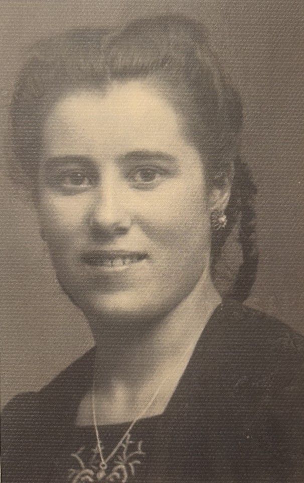 Black-and-white portrait of a woman with braided hair, wearing a dark top, earrings, and a necklace, facing the camera and smiling slightly.